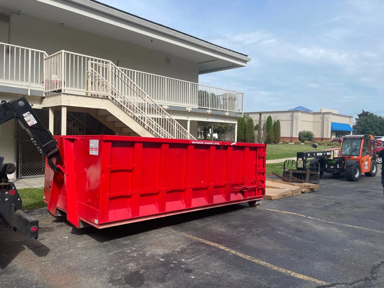 Red roll-off dumpster beside a building with construction equipment nearby