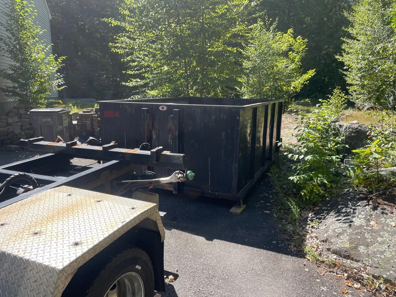 Dark roll-off dumpster on protective boards beside a driveway and delivery truck