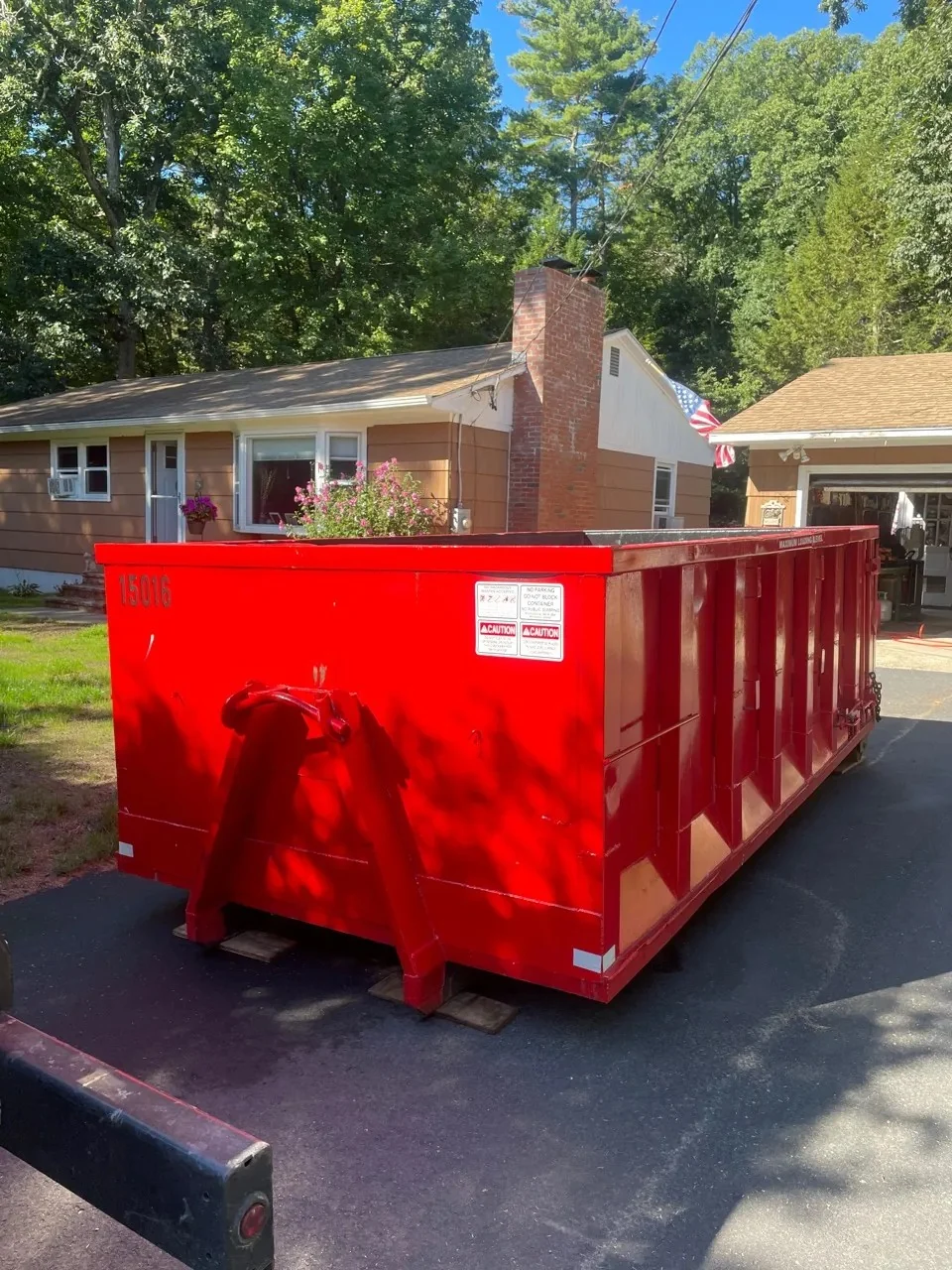 Red roll-off dumpster resting on protective boards in a residential driveway