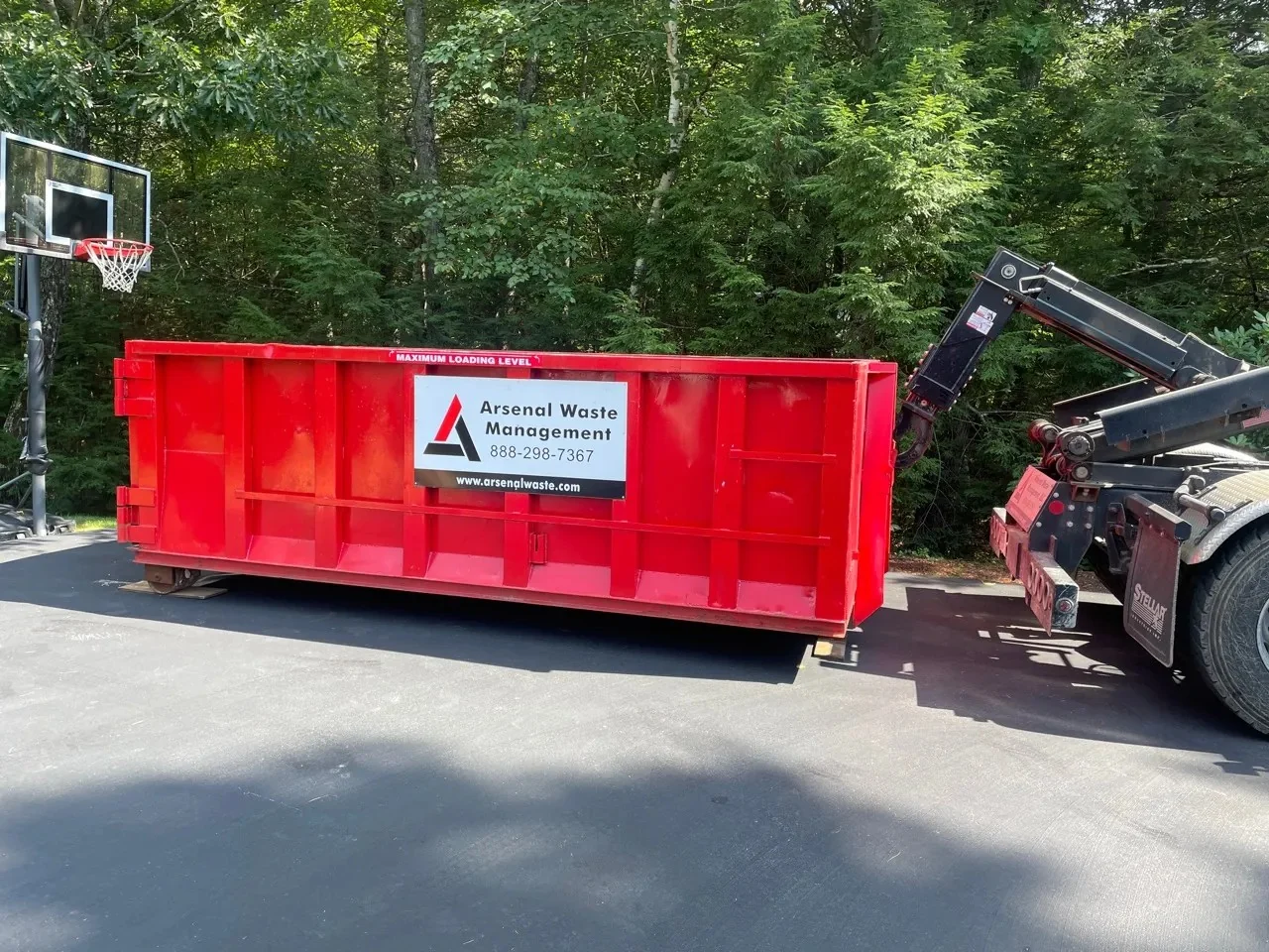 Red Arsenal Waste Management roll-off dumpster beside a delivery truck on a paved driveway
