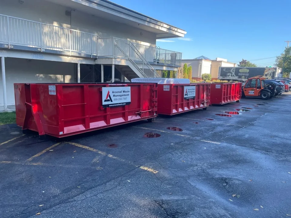 Three red Arsenal Waste Management dumpsters lined up beside a building